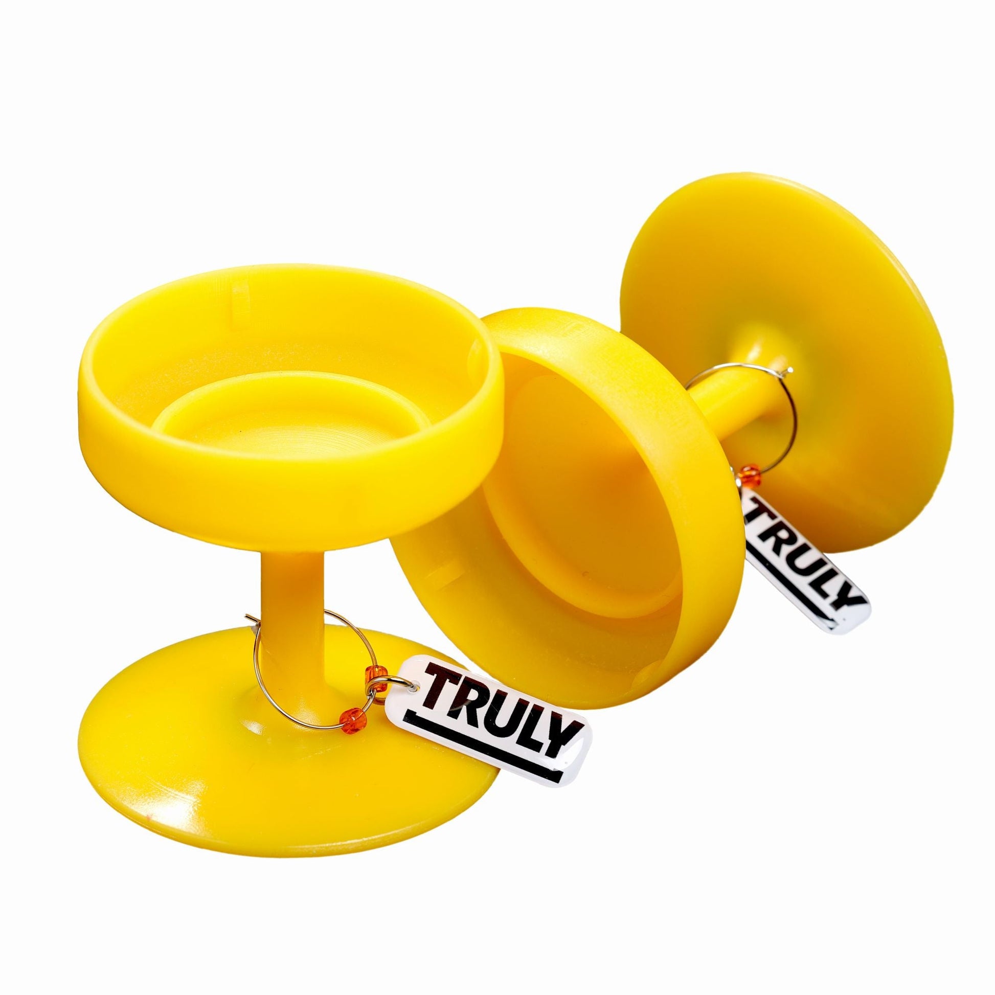 Two bright yellow plastic bases shaped like the bottom of stemmed glasses with "TRULY" tags, designed to hold Truly Hard Seltzer cans. One stands upright, and the other is lying on its side.
