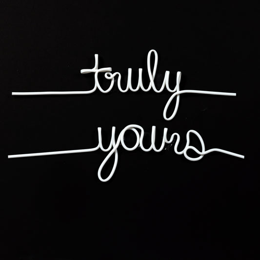 Two white, straws shaped to spell 'truly' and 'yours' in a handwritten script. The word 'truly' is on the top line, and 'yours' is on the bottom line. Both words have straight lines extending from their ends, suggesting they are meant to be drinking straws. The background is black