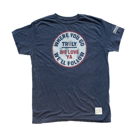 Front view of tee has large emblem in centered. Says "Where you go we'll follow" around the inside of the circle, and it the center is the truly logo and writing "We'll love ya".