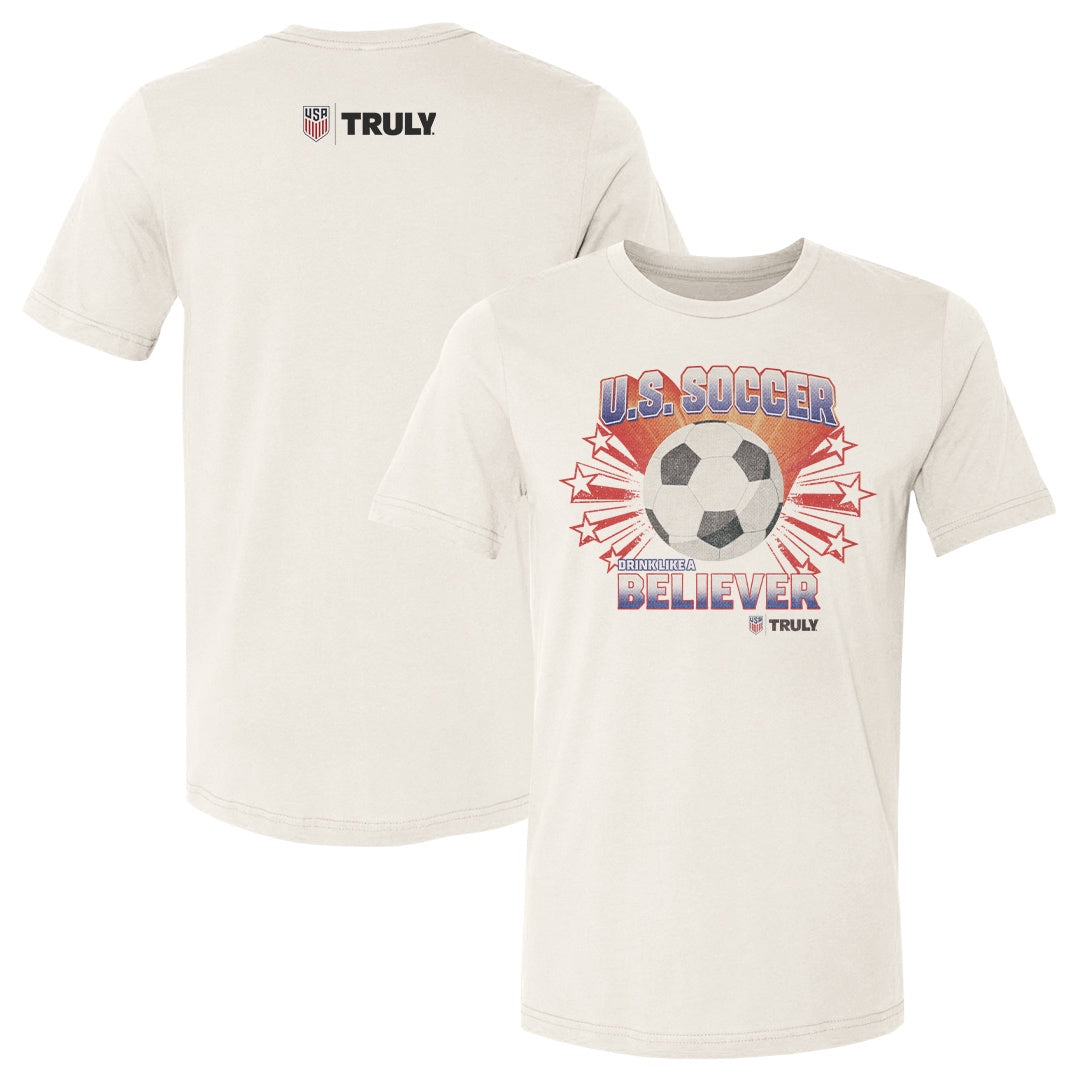 Cream colored tee shirt with a U.S. Soccer and Truly logo on the upper back. Front of tee shows a vintage graphic of a black and white soccer ball with red shooting stars coming out from behind, with text reading "U.S. Soccer"  on top, and "Drink Like A Believer" on the bottom of the graphic 