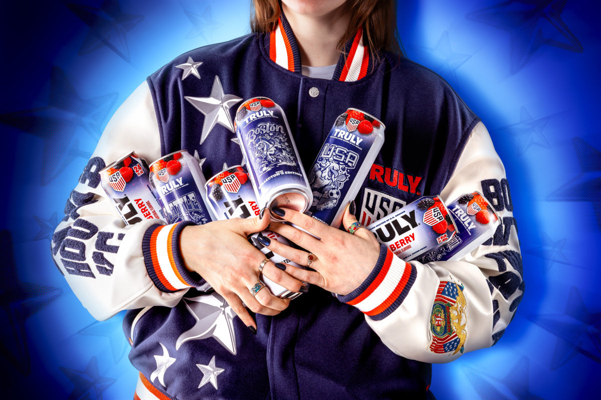 Styled action shot of a person wearing a varsity jacket holding several Truly USA baller berry cans